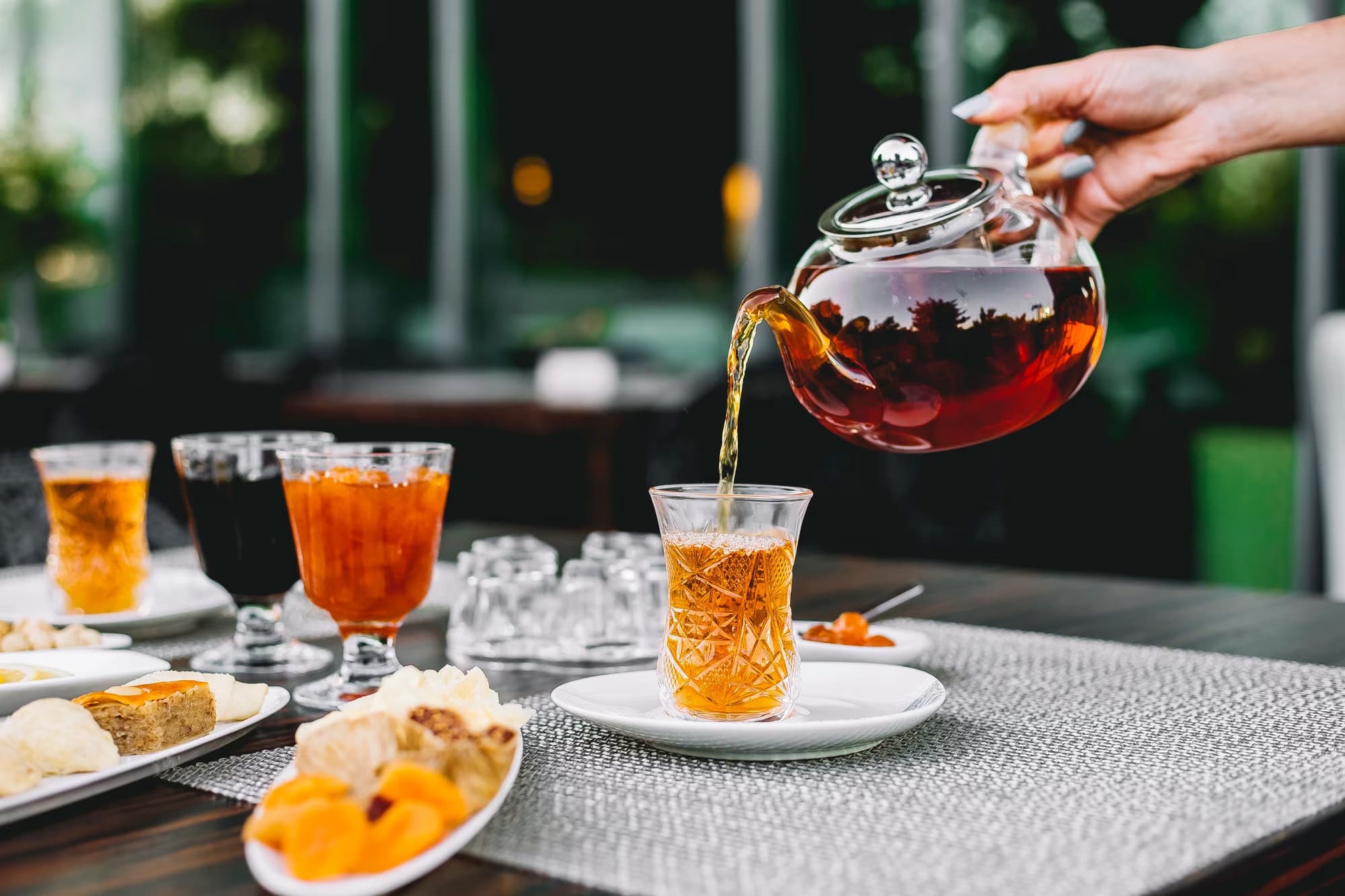 Front view of a girl pouring tea from a teapot, accompanied by a glass of jam and sweets on the table