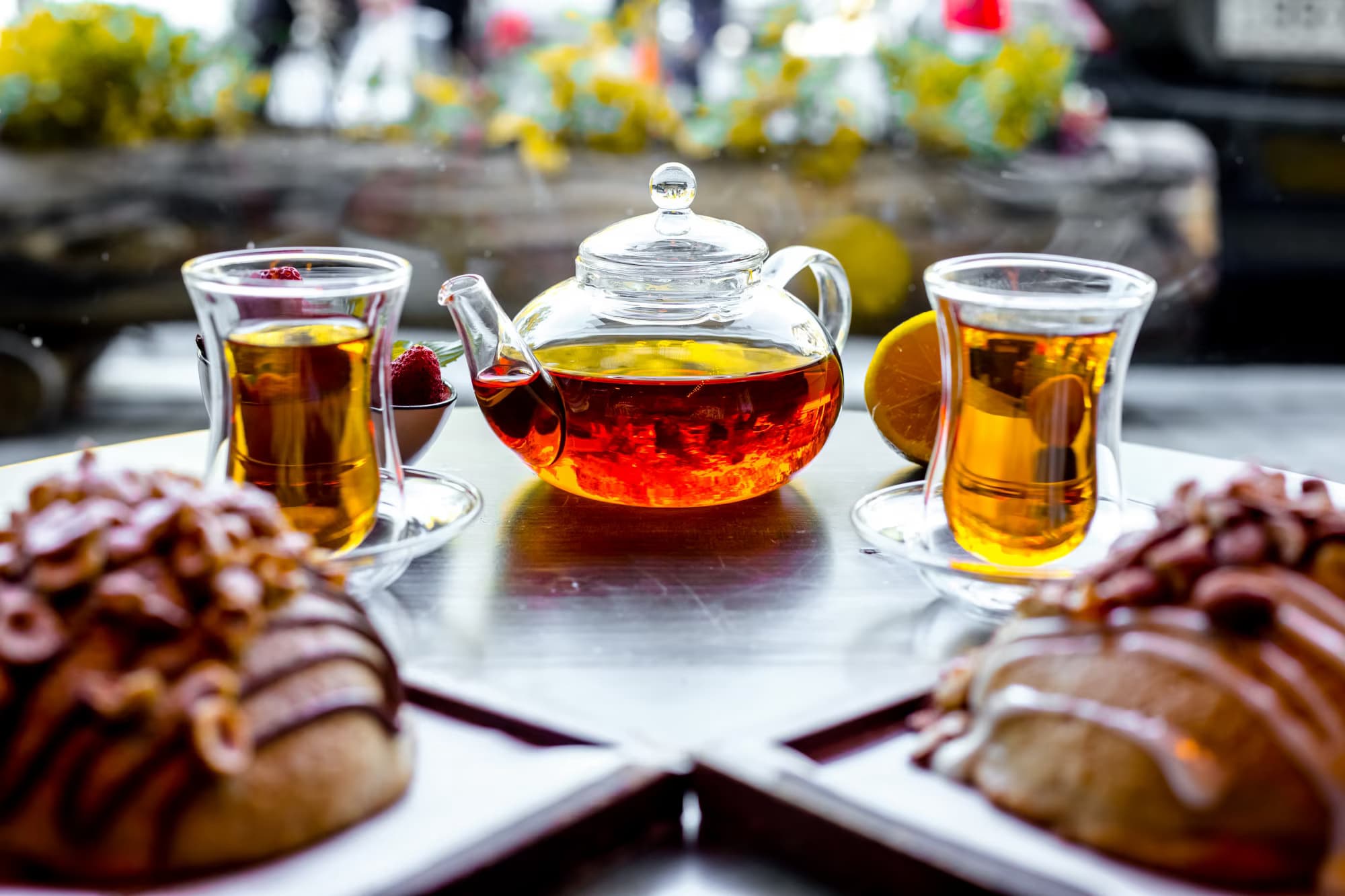 Front view of two buns with nuts and two armouda glasses of tea, accompanied by a tea kettle on the table