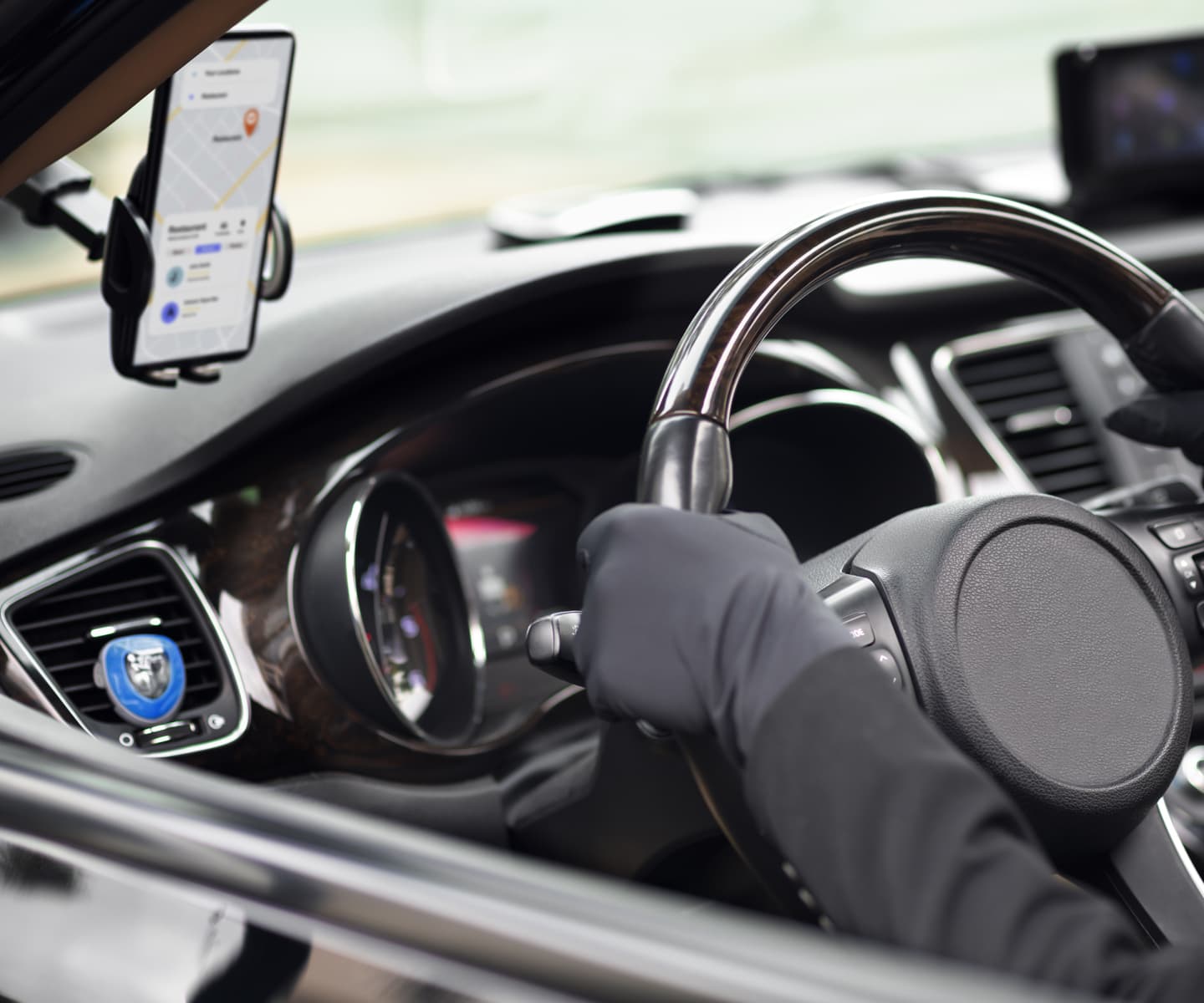 Car's front door showing steering wheel and driver using navigation on phone